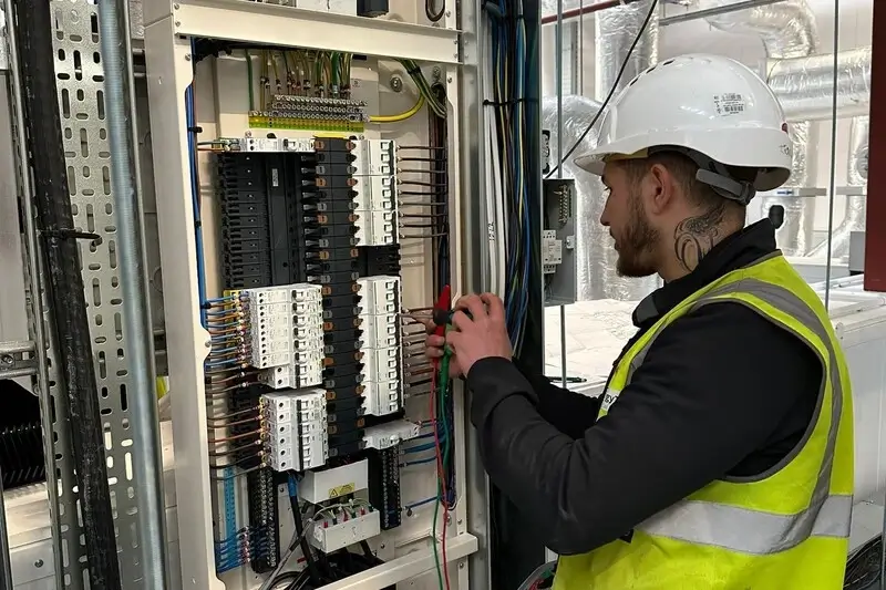 A man in a hard hat works on an electrical panel